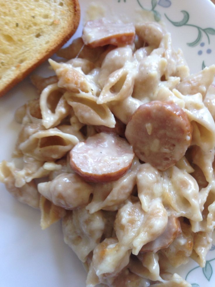 a plate with pasta and sausage on it next to a slice of toasted bread