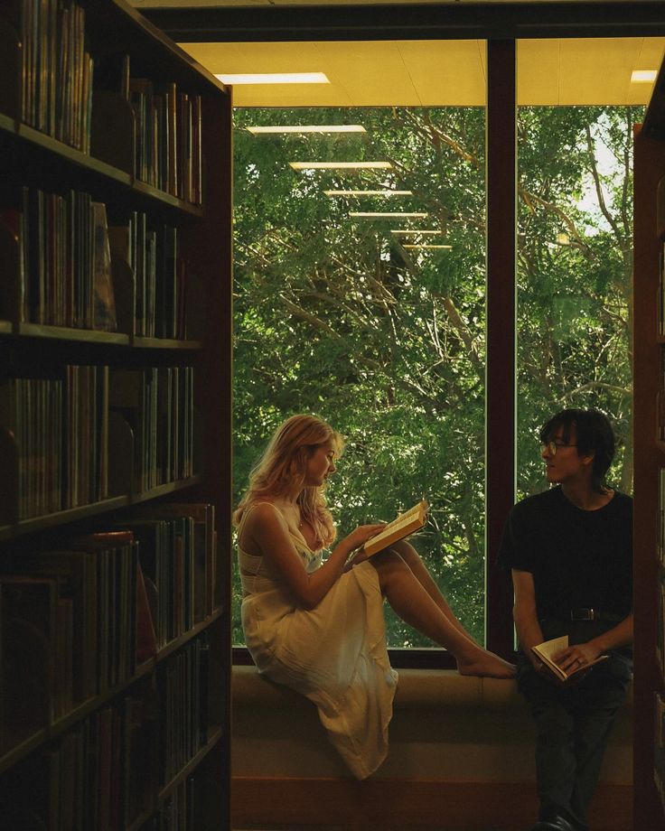 a man and woman sitting next to each other in a library with books on the shelves