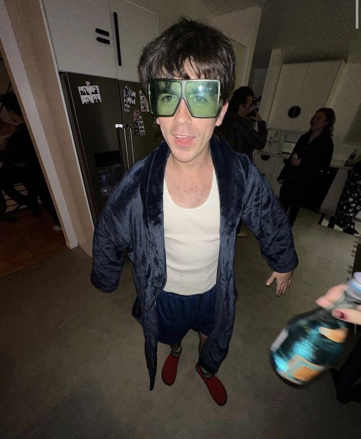 a man wearing sunglasses and holding a skateboard in his hand while standing on the floor