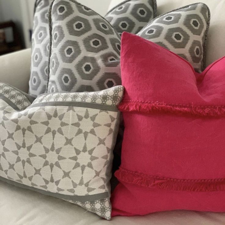 three pillows on a white couch with pink and grey accents, one in the middle