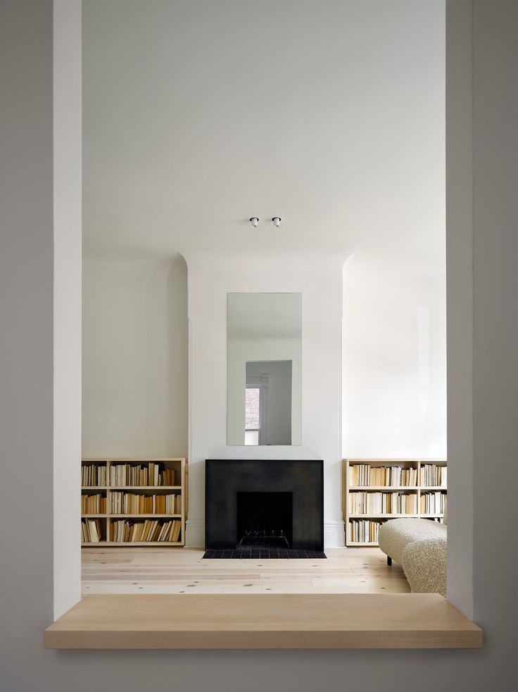 an empty room with bookshelves and a fireplace in the center, surrounded by white walls