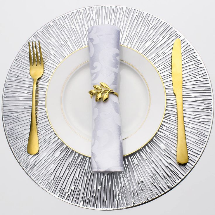 a white plate topped with a napkin next to a gold fork and knife set on top of it