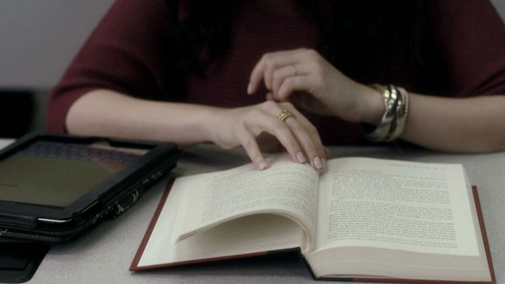 a woman sitting at a table with an open book in front of her and a cell phone