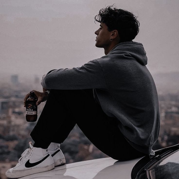 a man sitting on top of a car holding a bottle and looking at the city