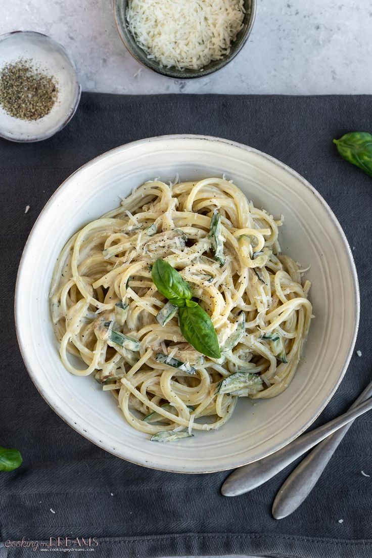 a white bowl filled with pasta and pesto on top of a black place mat