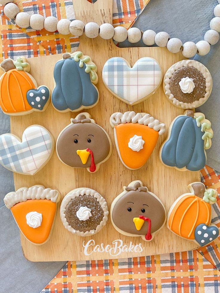 decorated cookies are arranged on a wooden board with plaid tablecloth and pumpkins in the background