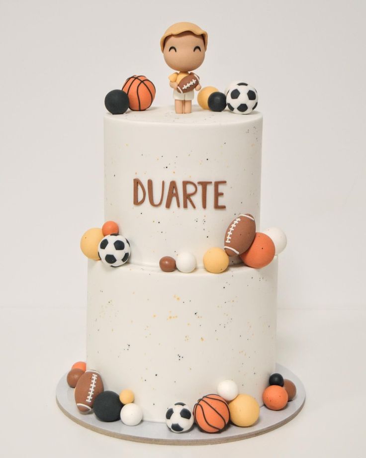 a white cake topped with lots of different types of balls and footballs on it