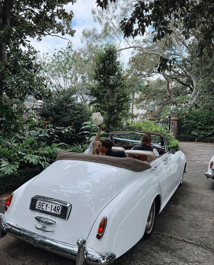 a white convertible car parked in front of a lush green tree filled park with lots of greenery