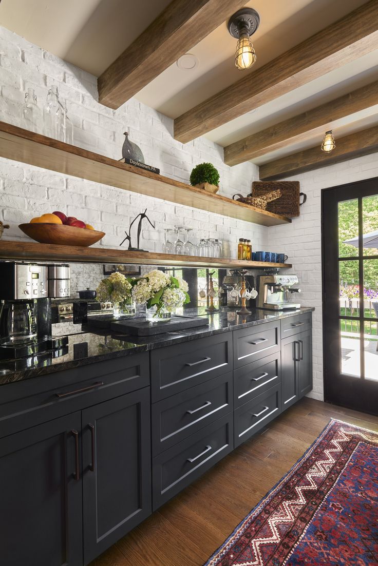 a kitchen with black cabinets and wooden shelves on the wall next to an open door