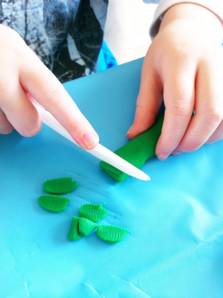 a child is cutting green plastic pieces with a toothbrush on a blue tablecloth