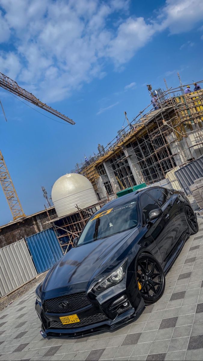 a black sports car parked in front of a building under construction with cranes behind it