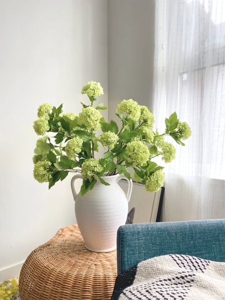 a white vase filled with green flowers sitting on top of a table next to a blue chair