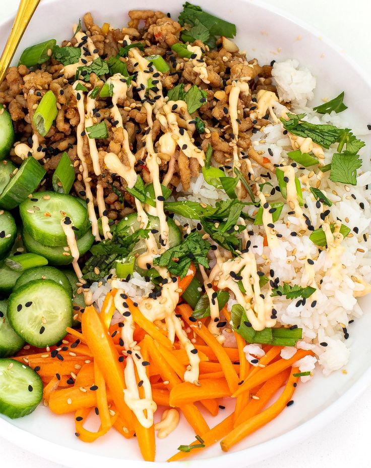 a white plate topped with rice, carrots and cucumbers next to chopsticks