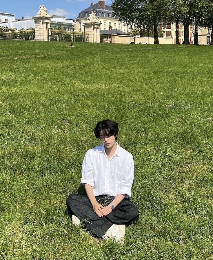 a man sitting in the middle of a field with his eyes closed and hands folded