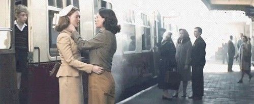 two women standing on the side of a train as people board it and talk to each other