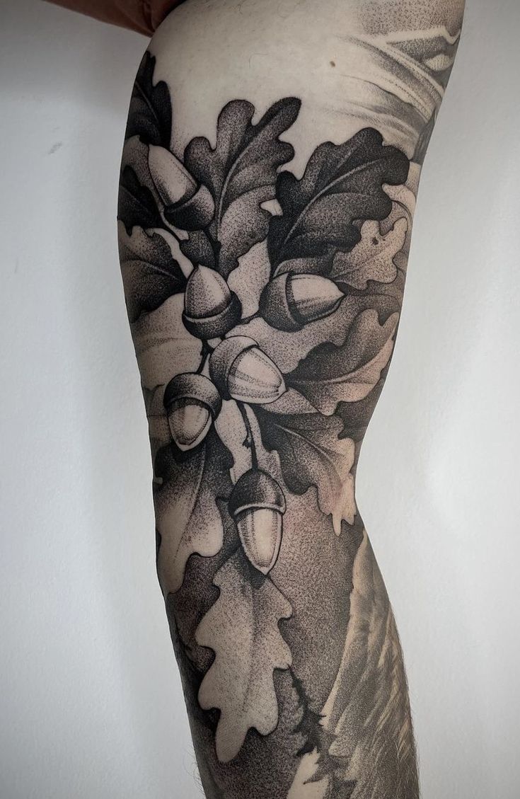 a man's leg with an oak and acorn tattoo design on the side