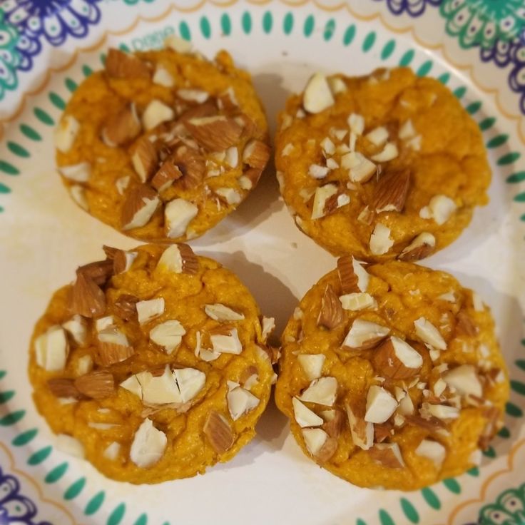 four cookies with nuts are on a colorful and patterned plate, ready to be eaten