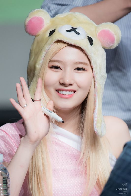 a girl with long blonde hair wearing a bear hat and holding her hand up in front of her face