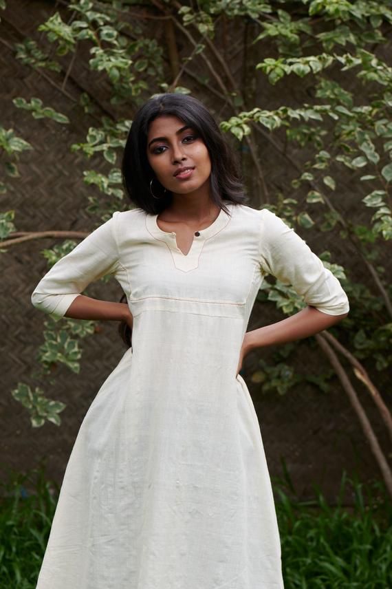 Rich buttery kora in a flared kurta with a shaped square yoke Length - 46 inchesHeight of model - 5'4" / 163cmMeasurements of model - 33.5 inch (bust) 28 inch (waist) 40 inch (hip)Model wears a size XSColour - Kora (off -white)Fabric - 100 % hand spun handwoven cottonCannot see throughCOMPOSITION100% pure cotton medium weight locally wovenTHE KAITHARI PROJECTHandspun, handwoven, designed and tailored in Kerala Traditional Fitted Kurta With Band Neckline, Off White Fitted Anarkali Kurta, Fitted Off White Anarkali Kurta, Off White Fitted Straight Kurta, Fitted Cream Kurta For Summer, Off White Fitted Long Sleeve Kurta, Fitted Long Sleeve Off White Kurta, Fitted Beige Anarkali Kurta, Fitted Cream Kurta For Spring