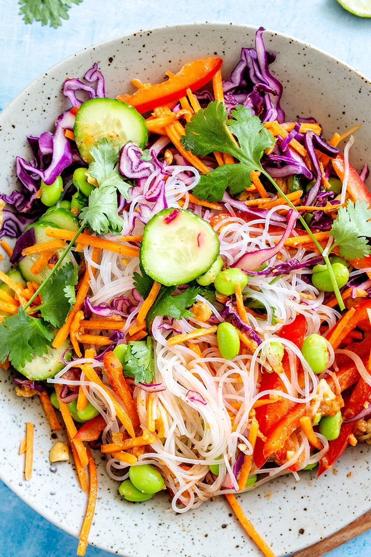 a salad with carrots, cucumbers and sprouts in a white bowl