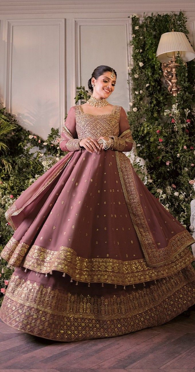 a woman in a pink and gold gown standing on a wooden floor with flowers behind her