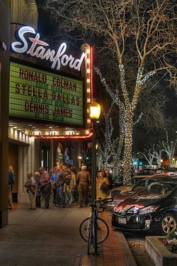 cars parked on the side of a street next to a movie theater sign with lights