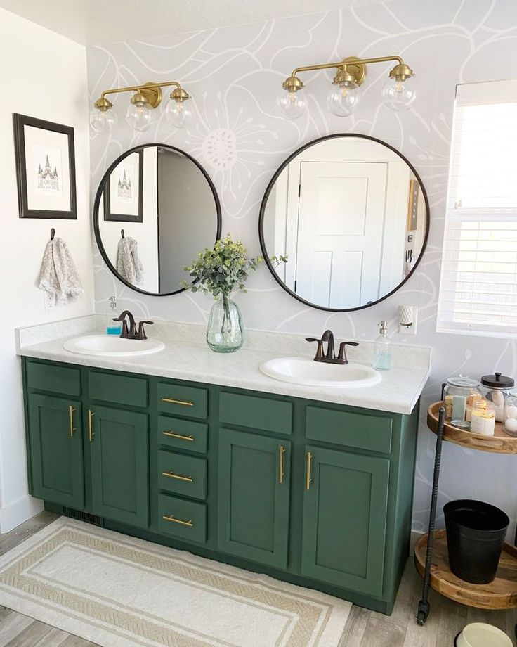 a bathroom with two round mirrors above the sinks and green cabinetry on the wall