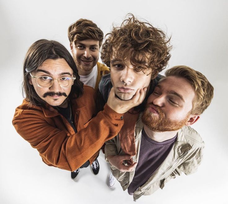 four men are posing for the camera with one man's face covered by his hands