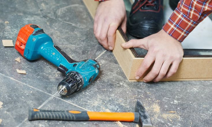 a man is working with tools on the floor in his home, he is using a drill