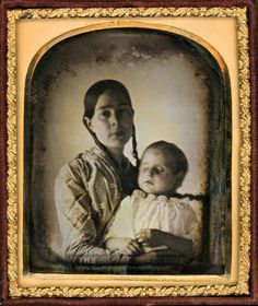 an old photo of a woman holding a baby in her arms and looking at the camera