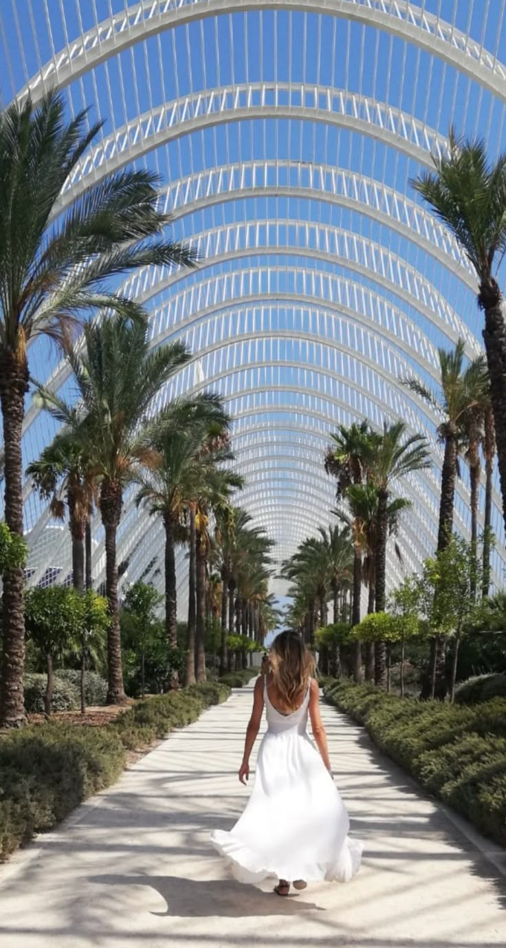 a woman in a white dress is walking down a walkway with palm trees and blue sky overhead