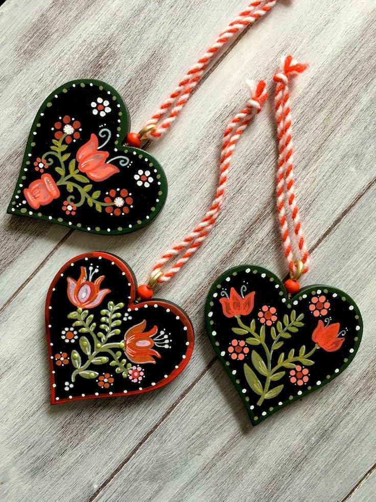 three heart shaped ornaments hanging from strings on a wooden surface with flowers and leaves painted on them