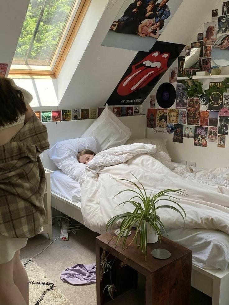 a woman standing next to a bed in a room with pictures on the wall above it