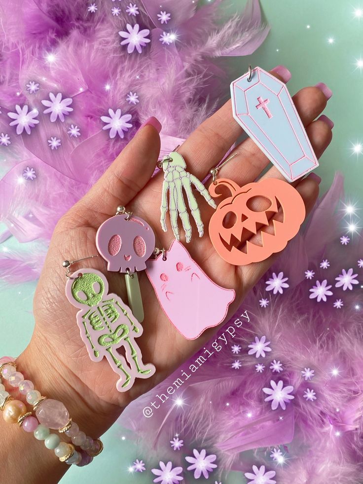 a hand holding several different colored and shaped halloween pins in it's palm, with purple flowers behind them