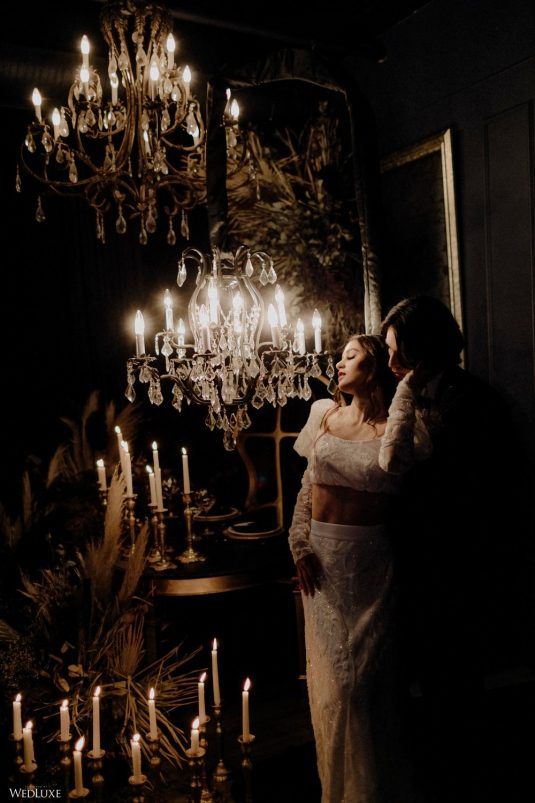 two people standing next to each other in front of a chandelier with candles