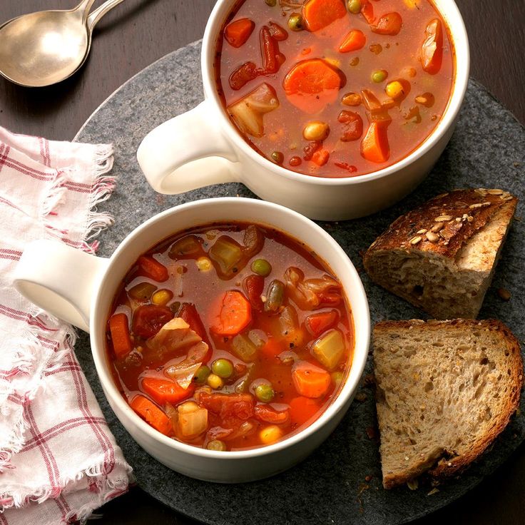 two bowls of vegetable soup on a plate with bread