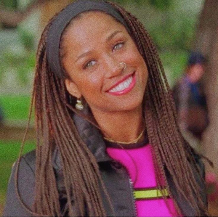 a woman with long dreadlocks smiles for the camera while standing in front of a tree