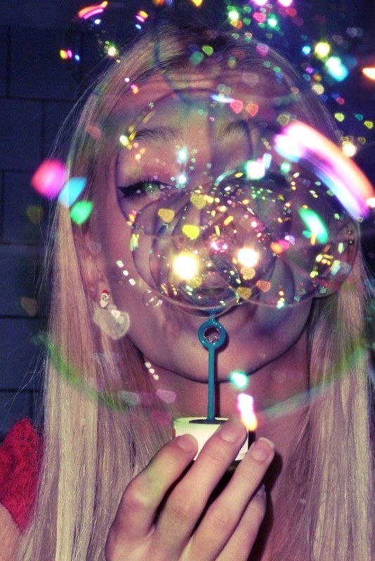 a woman blowing bubbles in the air while holding a small key to her face and looking at it