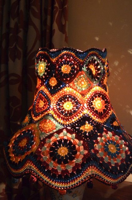 a crocheted lamp shade is sitting on a table next to a window curtain