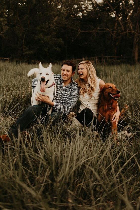 a man and woman sitting in tall grass with two dogs