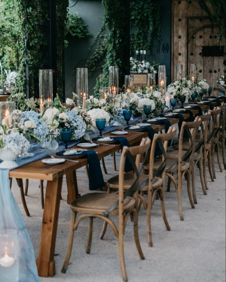 a long table is set up with blue and white flowers, candles, and napkins