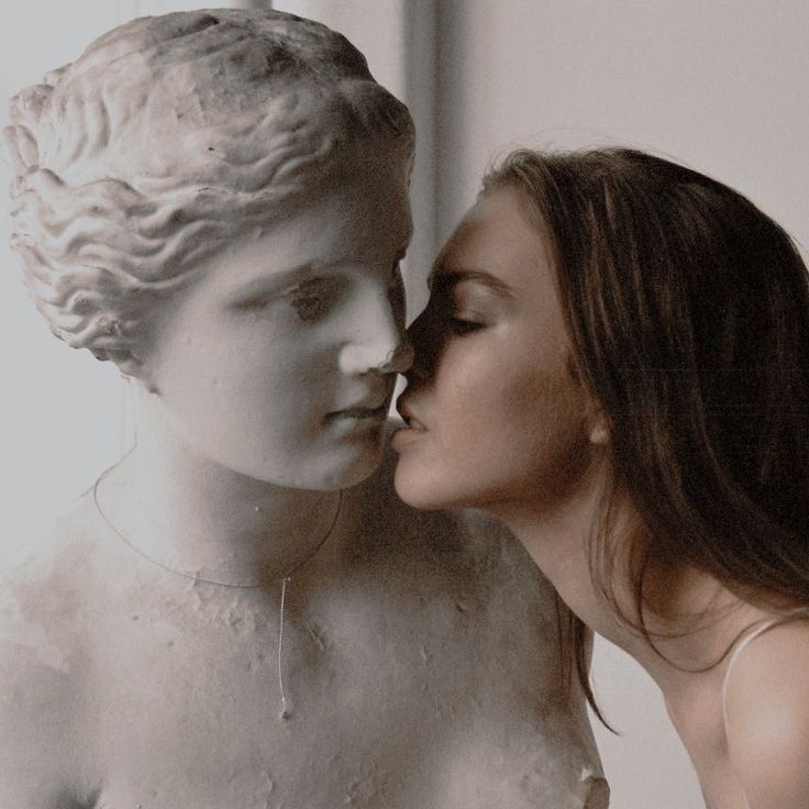 two women kissing each other in front of a statue