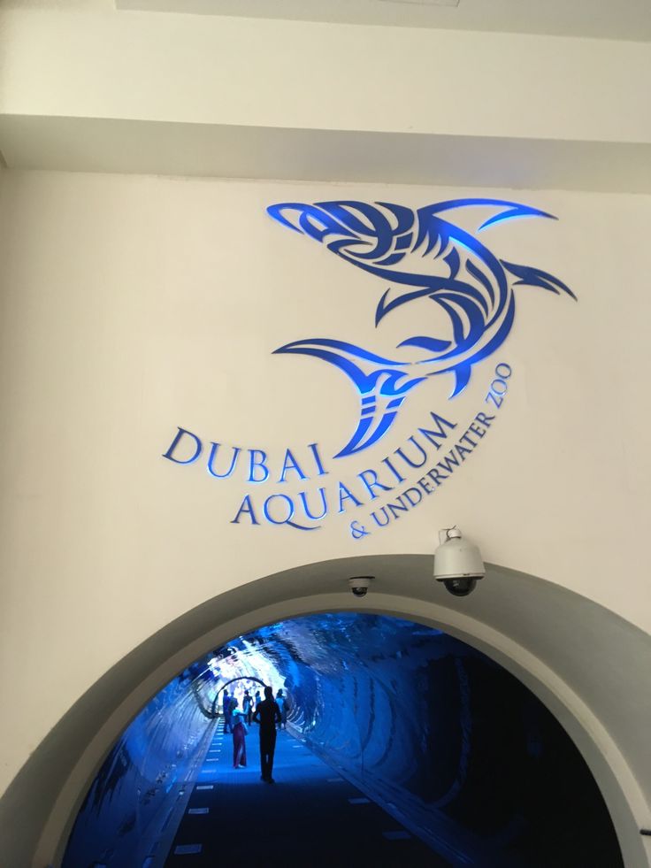 two people are walking through a tunnel under a sign that says dubai aquarium and underwater club