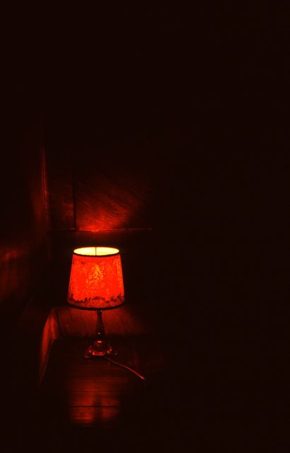 a red lamp sitting on top of a wooden table next to a wall with dark walls