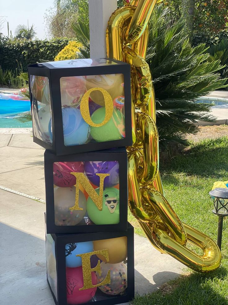 three boxes with balloons and letters on them sitting in front of a slide at a backyard party