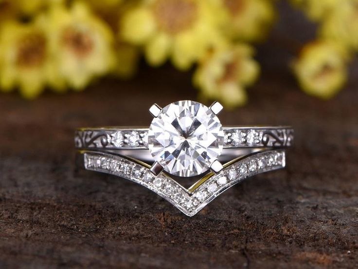 a close up of a diamond ring on a wooden surface with flowers in the background