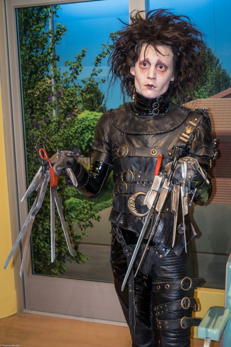 a woman dressed in black leather holding scissors and pliers with her hands out to the side