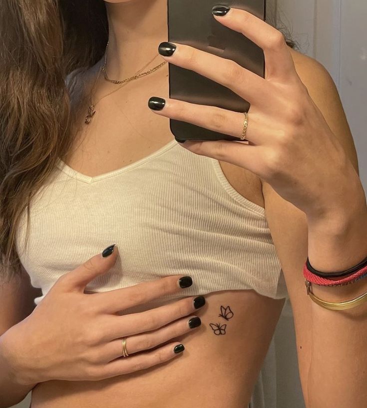 a woman holding up her cell phone in front of her stomach with tattoos on it