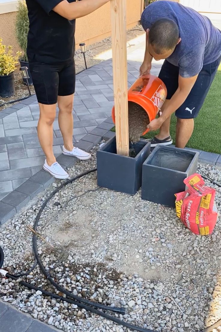 two men are working on a small fire hydrant in the back yard with gravel around it