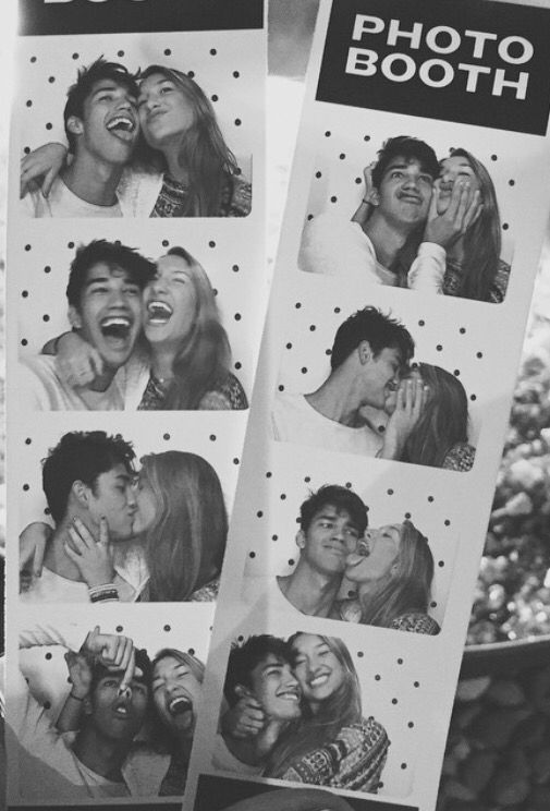 black and white photograph of people kissing in front of a photo booth sign that says photos booth